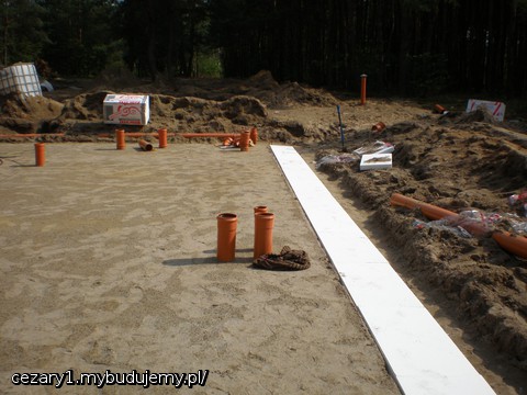 w trakcie układania izolacji przeciwwodnej/przeciw przemarzaniu wokół płyty fundamentowej ze spadkiem około 2% na zewnątrz od płyty fundamentowej. Górna płaszczyzna styropianów na jednym poziomie z wierzchnią warstwą podbudowy z pospółki (piasek rzeczny) zagęszczonej warstwami na przemian z piaskiem drobnoziarnistym z wykopu płyty fundamentowej - badanie geotechniczne wykazało, że stopień zagęszczenia jest odpowiedni i spełnia normę wyznaczoną przez projektanta.