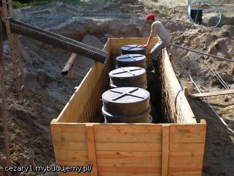 a to już poranek dnia następnego - czekam rozpoczęcie lania betonu z  gruszki do szalunku z oczyszczalnią. Niestety nie obyło się bez problemów przy betonowaniu, bo mimo dbałości o każdy szczegół z mojej strony, to nie ustrzegłem się drobnego, ale brzemiennego w skutki niedopatrzeń, mianowicie dystanse z kostki betonowej zostały przymocowane między zbrojeniem a szalunkiem, ale nie między zbrojeniem a oczyszczalnią, ponieważ myślałem, że wystarczy napełnienie zbiorników wodą w niemalże 3/4 objętości, nie wziąłem pod uwagę jednak tego, że beton lany z gruszki może swoją masą przesunąć zbiornik w szalunku - nawet napełniony wodą, co też się stało niestety. Akurat pompo-gruszka nawaliła i zgodziłem się na gruszkę bez pompy i to była kupa, bo gdyby była pompo-gruszka, to stopniowo zalalibyśmy zbiornik z każdej strony i nic by się nie działo:>. Jednak wspólnymi siłami poprawiliśmy ustawienie zbiornika i udało się go zabetonować; jest teraz tylko trochę przechylony na jedną stronę, ale to nie będzie przeszkadzać ani w działaniu oczyszczalni, ani wpływać na wygląd po zakopaniu, bo na kominy nałożone zostały betonowe kręgi - zdjęcia będą dodane wkrótce.